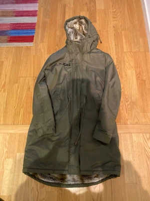Jacka khaki strl 40-42 som ny - Jacka i khaki färg med fuskpäls foder. Avtagbar luva. Parka model. Skick som ny!