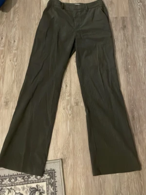 Gråa kostymbyxor  - Gråa lätt randiga kostymbyxor från Madlady i storlek 38. Dom har två fickor framtill och byxorna har en lösare form. Byxorna stängs med både knapp och två hakar