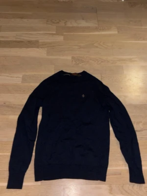 Mörkblå merinoulltröja Morris XS - Säljer en mörkblå tröja från Morris i 100% merinoull. Klassisk rund halsringning och diskret Morris-logga broderad på bröstet. Tröjan har lång ärm och ribbade muddar vid ärmslut och nederkant. Perfekt för dig som gillar stilrena och tidlösa plagg. Lite liten i storleken men passar fortfarande XS, pris kan diskuteras!