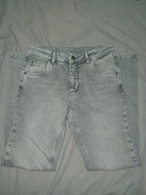 Jeans grå - Säljer ett par grå jeans med tvättad finish och klassisk femficksdesign. Jeansen har raka ben och normal passform, med bälteshällor och knappgylf. Perfekta för dig som gillar en enkel men stilren vibe.