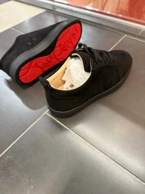 Svarta sneakers från Christian Louboutin - Säljer ett par svarta sneakers från Christian Louboutin i mocka med klassisk röd sula och diskret snörning. Skorna har en stilren design med rund tå och svarta detaljer. Perfekta för dig som vill ha något extra till din outfit.