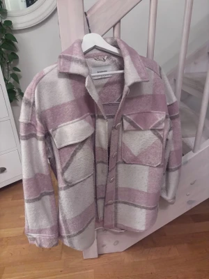 Rutig overshirt från Stradivarius - Säljer en supermjuk och mysig overshirt från Stradivarius i rutig design. Jackan är i ljusrosa och beige toner, har stora bröstfickor, knappar framtill och klassisk krage. Perfekt lager på lager-plagg för vår och höst.