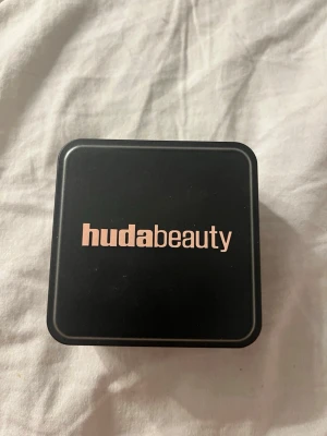 Huda Beauty Easy Bake Sugar Cookie puder - Lös baking & setting powder från Huda Beauty i nyansen Sugar Cookie. Kommer i en svart fyrkantig burk med lock. Perfekt för att fixera sminket och ge en matt finish. Innehåller 20g puder och är lätt att applicera under ögonen, T-zonen och hakan.