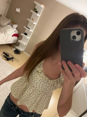 Prickig volangblus från Gina Tricot - Supersöt vit blus med svarta prickar från Gina Tricot. Toppen har volangkant vid ringningen, öppen rygg med knyt och är ärmlös. Materialet är lätt och luftigt, perfekt för varma dagar. ❣️har använt vid 1 tillfälle 