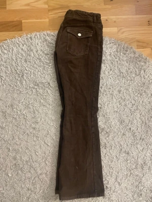 Bruna manchesterbyxor från H&M, 152 - Säljer ett par bruna manchesterbyxor från H&M i storlek 152. Byxorna har flared ben, medium midja och justerbar midja. Klassisk ficka med knapp bak och mjukt manchestertyg i bomull med lite stretch. Perfekta för dig som gillar retrovibbar och sköna material.