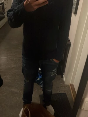 Mörkblå kabelstickad tröja Selected Homme - Säljer en mörkblå kabelstickad tröja från Selected Homme. Tröjan har rund halsringning, ribbade muddar och nederkant samt ett klassiskt kabelmönster över hela plagget. Perfekt för dig som gillar stilrena och tidlösa plagg.