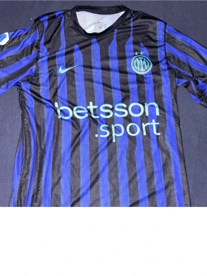 Inter Milan randig Nike matchtröja - Säljer en Inter Milan matchtröja från Nike med blå och svarta ränder, broderad klubbmärke och Nike-logga. Tröjan har sponsortryck på bröstet och spelarnamn samt nummer 20 på ryggen. Tillverkad i lätt polyester, perfekt för fotbollsplanen.