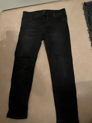 Jack and Jones Svarta Slim/Glenn jeans 29/30 - Säljer ett par svarta Slim/Glenn jeans från Jack & Jones i storlek 29/30. Jeansen har en slim passform, klassisk femficksdesign och knäppning fram. Materialet är mjukt och stretchigt jeans-tyg som sitter snyggt längs benen. Använd en gång så i nyskick