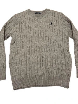 Grå kabelstickad tröja Polo Ralph Lauren - Säljer en grå kabelstickad tröja från Polo Ralph Lauren. Tröjan har rund hals, lång ärm och den klassiska broderade loggan på bröstet. Perfekt för dig som gillar en clean och tidlös stil. Passar till allt och är superenkel att matcha.
