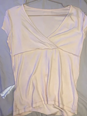 Ljusbeige omlottopp med v-ringning - Säljer en ljusbeige omlottopp i mjukt material med korta ärmar och snygg v-ringning. Toppen har synliga sömmar och en avslappnad passform som gör den enkel att styla till olika looks.