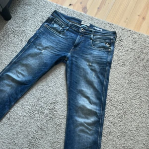 Replay Anbass slim fit jeans blå - Snygga blå Replay Anbass jeans i slim fit med klassisk femficksdesign och coola slitningar. Jeansen har dragkedjegylf, läderpatch bak och kontrastsömmar. Tillverkade i stretchig bomullsdenim för skön passform. Skriv vid minsta funderingar. Nypris runt 2000 mitt bara 899