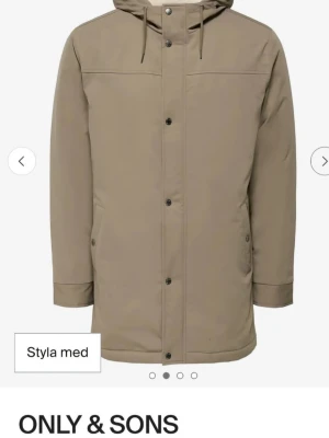 Beige parkasjacka från ONLY & SONS - Säljer en beige parkasjacka från ONLY & SONS med huva och dragsko. Jackan har knappar framtill, två fickor med lock och en rak, längre passform. Perfekt för kyligare dagar och enkel att matcha med olika outfits.