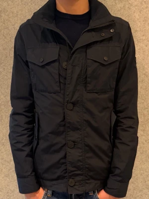 J.Lindeberg Bailey Poly Field Jacket - Tjena, säljer denna tvärfeta Lindeberg bailey jackan i marinblå färg. Jackan passar storlek S dock står det XS på jackan. Jackan är knappt använd, och passar perfekt nu inför våren. Skriv gärna vid intresse!