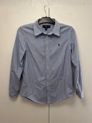 Randig Ralph Lauren skjorta - Klassisk skjorta från Ralph Lauren med blå/vita ränder. Inga slitage täcken. Skick 10/10. Storlek 18 som motsvarar S. Pris ej hugget i sten. 