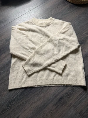 Ljusbeige stickad tröja med rund hals - Mysig ljusbeige stickad tröja med rund hals och ribbade muddar. Tröjan har en avslappnad passform och är perfekt för kyligare dagar. Enkel och stilren design som funkar till allt.