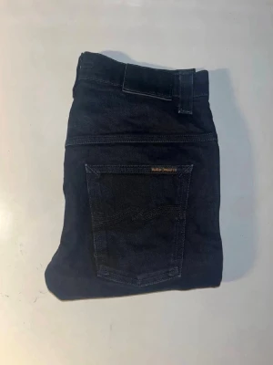 Svarta Nudie Jeans  28/32 - Säljer ett par svarta jeans från Nudie Jeans. Storlek 28/32. De har en smal passform med avsmalnande ben, klassiska fem fickor och snygga sömmar på bakfickorna. Tillverkade i ekologisk bomull med lite stretch för extra komfort. Hör av dig om du har några frågor🙌