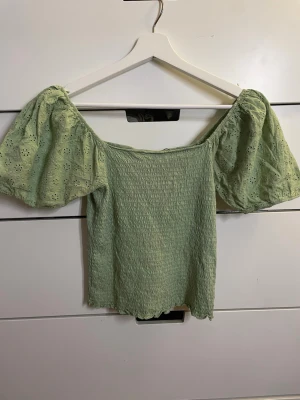 Grön blommig offshoulder topp Dobber - Säljer en ljusgrön offshoulder topp från Dobber i storlek S. Toppen har puffiga korta ärmar med broderade blommor och smockad kropp. Perfekt inför våren och ger en söt och trendig look. Övre sömmen vid halsen har släppt lite, går att fixa enkelt och märks inte när man bär tröjan!