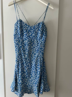 Blommig blå kortklänning från Zara - Supersöt blå kortklänning från Zara med vita små blommor och tunna axelband. Liten i storleken, skulle mer säga att den är en S. 