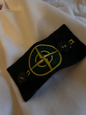 Vit jacka från Stone Island - Säljer en clean vit jacka från Stone Island med den klassiska svarta patchen och gult/grönt broderat kompassmärke på ärmen. Jackan har en stilren look och passar perfekt till streetwear. Materialet känns mjukt och följsamt.