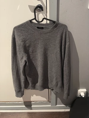 Grå stickad tröja Massimo Dutti - En enkel och stilren grå ganska tjock stickad tröja från Massimo Dutti. Tröjan har rund halsringning, ribbade muddar och är långärmad. Perfekt för lager på lager under kyliga dagar. Storlek är L men sitter mer som M.