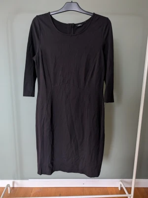 Svart långärmad klänning från Lindex - En stilren svart klänning från Lindex med lång ärm och figurnära passform. Klänningen har rund halsringning och dragkedja i ryggen. Tillverkad i mjukt material som känns bekvämt mot huden. Perfekt för dig som gillar enkel och klassisk stil.