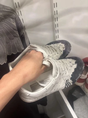 Vita sneakers med svart färgstänk - Unika vita sneakers från Publica med svart färgstänksmönster över hela skon. Klassisk låg modell med snörning och rund tå. Tillverkade i textilmaterial för en avslappnad och cool look. Perfekta för dig som vill sticka ut med din stil.