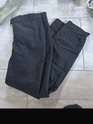 Svarta kostymbyxor med raka ben - Säljer ett par klassiska svarta kostymbyxor med raka ben och bälteshällor. Byxorna har en stilren look och passar perfekt till skjorta eller t-shirt. Materialet känns mjukt och följsamt, vilket gör dem sköna att bära hela dagen.
