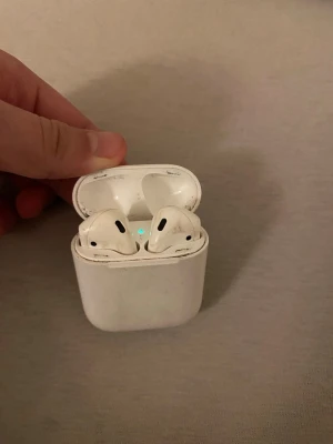 Apple AirPods (2nd generation) - Apple AirPods (2nd gen) med laddningsetui. Trådlösa hörlurar med smidig anslutning till iPhone och andra Apple-enheter. Synligt slitage och smuts på både hörlurar och etui, men fungerar som de ska. Perfekt för dig som vill ha äkta AirPods till ett bra pris. Dem båda funkar
