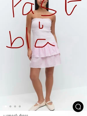 Ljusrosa axelbandslös kortklänning - Söt axelbandslös kortklänning i ljus blå/blå och vitt med smockad överdel och volang i kjolen. Klänningen har ett diskret mönster och är perfekt för varma dagar. Materialet känns lätt och luftigt.