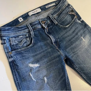 Replay Anbass Jeans - Snygga Replay Anbass jeans i blå tvätt med slitna detaljer och klassiska fem fickor. Skinny fit med låg midja och dragkedja. Materialet är stretchigt jeans för skön passform. Perfekta för dig som gillar en modern och avslappnad stil. Storlek: 29,32