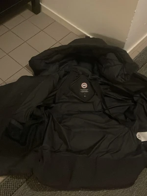 Svart pufferjacka från Canada Goose - Svart pufferjacka från Canada Goose i storlek M. Jackan har huva, dragkedja och knappar framtill, samt breda quiltade sektioner som ger en schysst look. Perfekt för kalla dagar med sin dunfyllda insida och stilrena design Pris kan diskuteras perfekt kondition. 