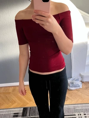 Vinröd offshoulder topp från H&M - Snygg vinröd offshoulder topp från H&M i storlek XS. Modellen är tight och croppad med korta ärmar som sitter precis ovanför armbågen. Mjuk och stretchig bomull som känns skön mot huden. Perfekt för dig som gillar stilrena och enkla plagg med lite edge.