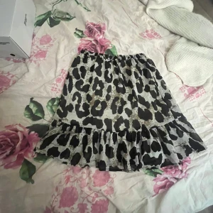 Leopardmönstrad volangkjol - Säljer en kort kjol med leopardmönster i svart och beige. Kjolen har volanger och en luftig, flowy passform med resår i midjan. Perfekt för dig som gillar att sticka ut med djurmönster och vill ha en trendig look.