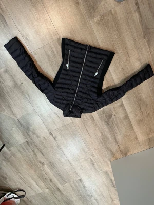 Svart pufferjacka från Softy, S - Svart pufferjacka från Sofity Love Collection i storlek S. Jackan har quiltad design, två dragkedjeförsedda fickor framtill och hel dragkedja. Långärmad och med smal passform, perfekt för kyliga dagar. Materialet är syntet och polyester.