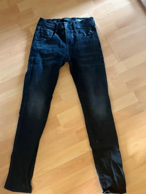 Replay Anbass svarta slim jeans - Säljer ett par svarta Replay Anbass jeans med slim fit. Jeansen har klassisk femficksdesign, normal midja och smala ben. Materialet är mjukt och stretchigt jeans, vilket gör dem riktigt sköna att bära. Perfekta för dig som gillar en clean och modern look.