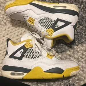Nike Air Jordan 4 Retro Vit/Gul 38 - Nike Air Jordan 4 Retro sneakers i vit skinn med detaljer i gul och svart. Klassisk meshpanel på sidorna, snörning och platt sula. Ikonisk Jumpman-logga på plösen och gul vadderad insida. Perfekt för dig som vill sticka ut med färg och stil.