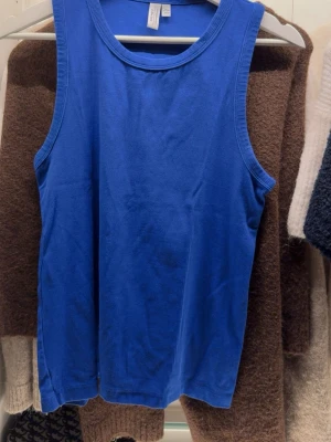 Blå linnetopp från & Other Stories - Säljer en klarblå linnetopp från & Other Stories, Stockholm Atelier. Toppen är ärmlös med rund hals och ribbade kanter. Materialet är mjuk bomull som känns skönt mot huden. Perfekt för dig som gillar enkla och stilrena plagg med färg.