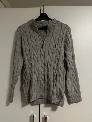 Knitwear från Polo Ralph Lauren - Grå Knitwear från Polo Ralph Lauren med klassisk rund hals och lång ärm. Diskret röd Polo-logga broderad på bröstet. Mjuk och skön ullskvalitet, perfekt för chill dagar. Stilren och enkel design som funkar till jeans