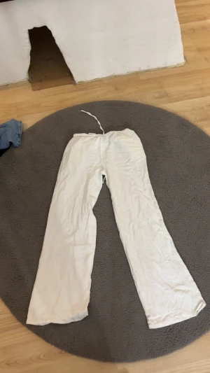 Vita linnebyxor med snörning - Säljer ett par vita linnebyxor med rak passform och snörning i midjan och har fickor på sidorna. Byxorna har en avslappnad look och är perfekta för varma dagar. Materialet är lätt och luftigt linne, vilket gör dem sköna att bära.