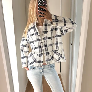 Rutig overshirt från Eila Helen - Säljer en vit och mörkblå rutig overshirt från Eila Helen. Jackan har en loose passform, stora fickor framtill och knappar längs hela framsidan. Materialet är grovt vävt och känns riktigt chill. Perfekt att slänga över en t-shirt för en cool look. Passar en S men är L