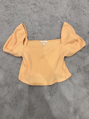 Ljusorange ribbad topp med puffärm från H&M - Säljer en ljus orange ribbad topp från H&M med snygga puffärmar och fyrkantig halsringning. Helt oanvänd.