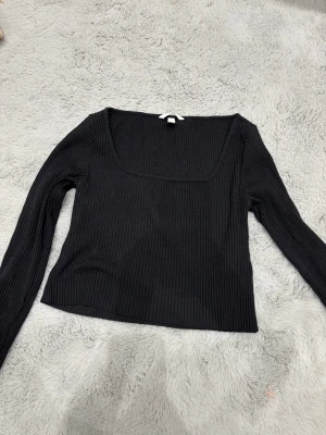 Svart ribbad långärmad topp - Säljer en svart långärmad topp med fyrkantig ringning och ribbad struktur. Endast använd ett fåtal gånger