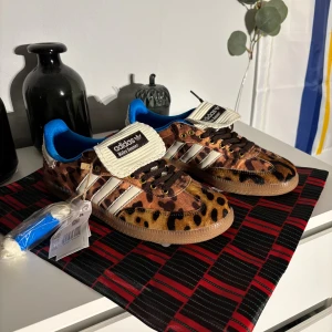 Adidas Wales Bonner leopard sneakers - Unika Adidas Wales Bonner sneakers med leopardmönster i bruna och beige toner, blå innersula och vita detaljer. Skorna har snörning, gummisula och klassiska Adidas-stripes på sidan. Materialet är syntet och skinn, med coola guldfärgade öljetter och Wales Bonner branding på plösen.