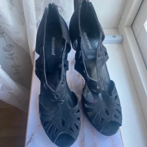 Svarta klackskor från Graceland - Säljer ett par svarta klackskor från Graceland med snygga utskurna detaljer och öppen tå. Skorna har en hög klack och dragkedja baktill för enkel på- och avtagning. Materialet är mocka och designen är riktigt stilren och edgy.knappt använda. Hämtas i norsborg botkyrka 