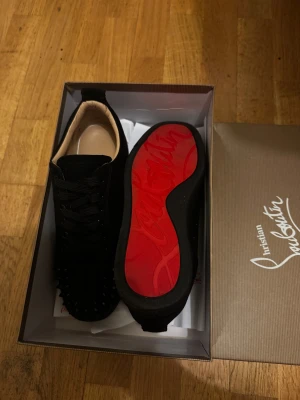 Christian Louboutin svarta  - Svarta sneakers från Christian Louboutin med ikonisk röd sula och svarta nitar på tån. De är köpta i april 2025 på farfetch för 9468 kvittot finns och de har använt få tal gånger  det är min ex skor och behöver inte de längre det är därför de säljs 😊😅