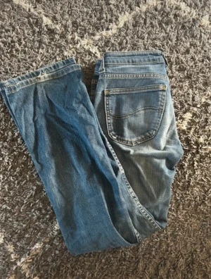 Blå bootcut jeans från Lee - Snygga blå jeans från Lee med klassisk bootcut passform och normal midja. Jeansen har midjemåttet 36 rakt över och Inrebenslängd 73