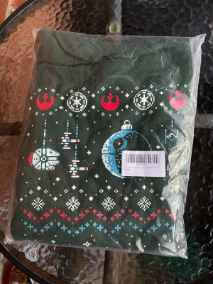 Ny Grön jultröja tröja med Star Wars motiv. Strl XL - Säljer en mörkgrön jultröja med Star Wars-motiv i pixelstil. Tröjan har lång ärm och tryck med Dödsstjärnan, Millennium Falcon, stormtroopers och juliga detaljer i rött, blått och vitt. Perfekt för dig som vill sticka ut på julmyset med nördiga vibbar.