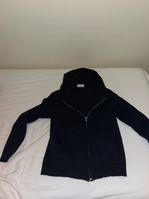 Svart hoodie från Rovoir Sweden - Svart hoodie från Rovoir Sweden i storlek S. Tröjan är stickad med dragkedja framtill, huva och två fickor. Materialet känns mjukt och passar perfekt för kyliga dagar. Långärmad och stilren design som funkar till många olika looks. Haft ett hål på ärmen men är lagat. Se bild 3. Skick 6/10 