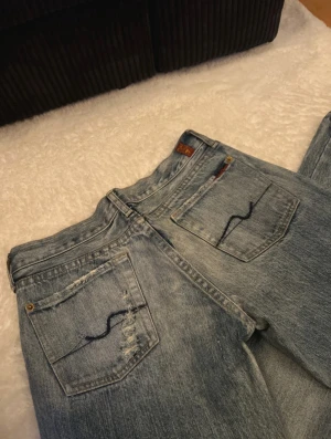 7 for all mankind  jeans ljusblå bootcut - Säljer ett par 7 for all mankind jeans i ljusblå tvätt med klassisk bootcut-passform. Jeansen har snygga slitningar och broderad på bakfickorna. Materialet är slitstarkt denim och modellen har normal/låg midja. Midjemått: 38 innerbenslängden:80