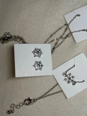 Snöflinge-Smyckeset – Halsband, Armband,berlock & Örhängen - Vackert vintrigt smyckeset i silverton med gnistrande snöflingor. Innehåller halsband, armband,berlock och örhängen – allt helt nytt. Perfekt som julklapp eller present under vintersäsongen.  💰 Nypris: ca 149–249 kr per del (värde ca 700–800 kr totalt).
